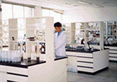 흰색 가운을 입은 실험자가 하얀 장식장으로 놓여진 연구실 안에서 실험을 하고 있다.