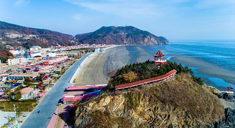 넓은 해변가와 연결된 조그만한 산 정상에 빨간색 정자가 세워져 있는 모습