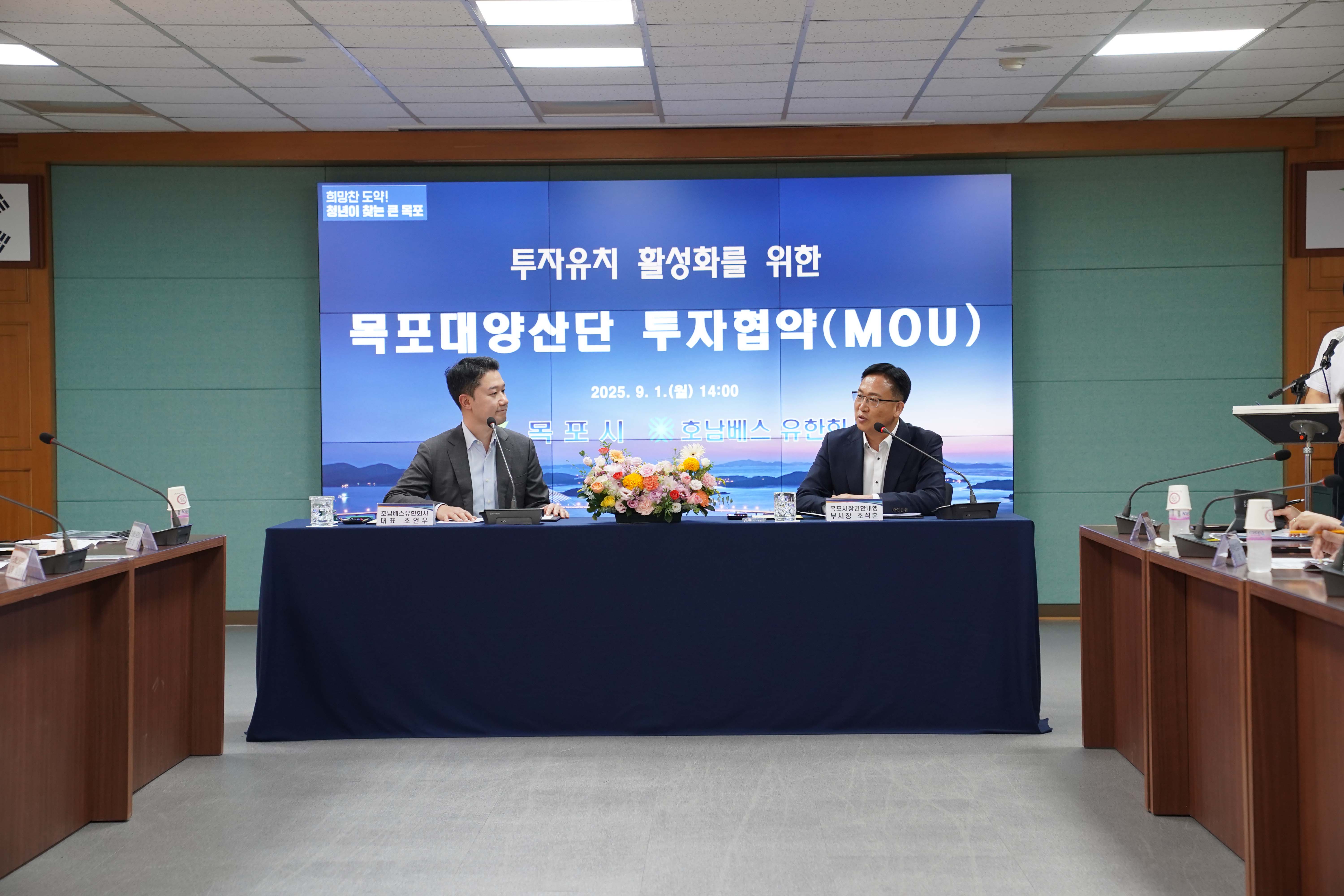 대형 스크린에 '투자유치 활성화를 위한 목포대양산단 투자협약(MOU)', '2025. 9. 1.(월) 14:00', '목포시, 호남베스 유한회사' 문구가 띄워진 회의실 전경. 테이블에는 '호남베스유한회사 대표 조언우'와 '목포시장권한대행 부시장 조석훈' 명패가 놓여 있으며 두 사람이 마주 보고 앉아 있음.