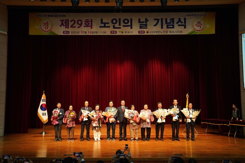 노인의 날 기념식에서 수상자들이 꽃다발을 들고 무대 위에서 단체 기념 촬영을 하고 있는 모습이다.