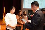 정장 차림의 관계자가 흰색 상의를 입은 여성 수상자에게 패를 전달하며 읽고 있는 모습이다.