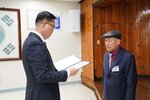 11월 정례조회로 정장을 입고 안경을 쓴 남성이 머리에 모자를 쓰고 짙은 네이비색 정장을 입은 국현근 수상자에게 상장을 수여 하고 있다.