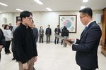 2026년 상반기 4급이하 정기인사로 정장을 입고 안경을 쓴 남성이 실내 행사장에서 한 남성에게 상장을 전달하며 내용을 읽고 있고, 남성은 검은 자켓을 입고 서 있으며 뒤쪽에는 참석자들이 줄지어 서서 행사를 지켜보고 있다.